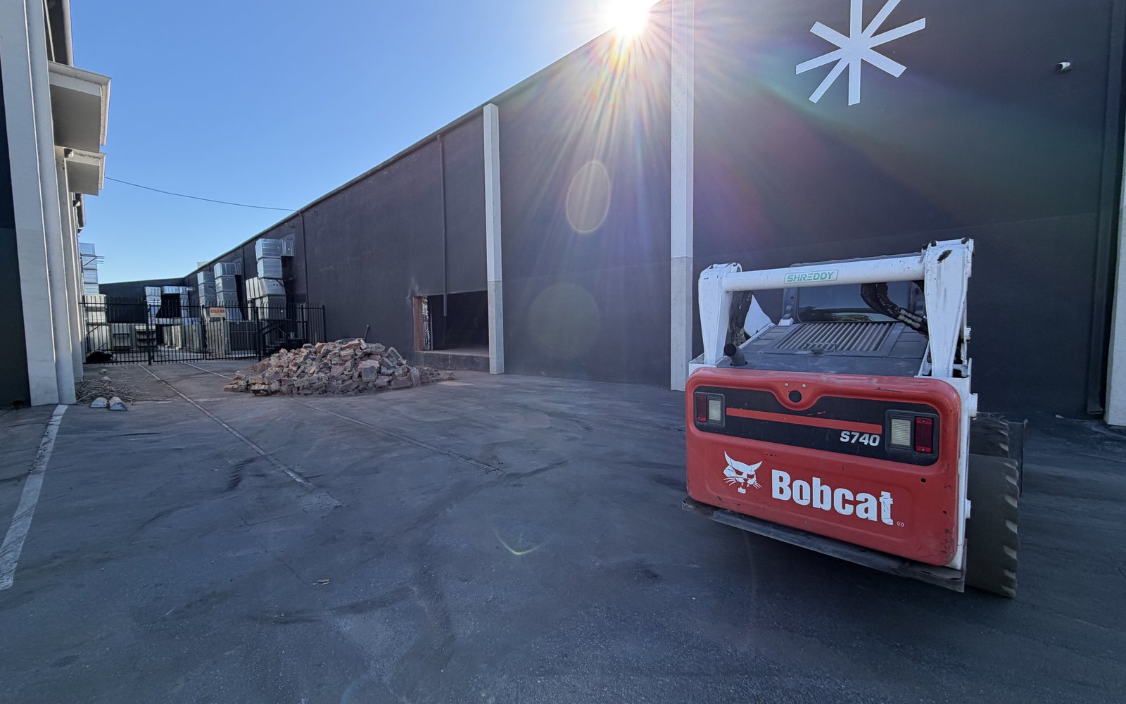 Bobcat S740 skid steer parked outside the warehouse beside a pile of cut concrete, sun flare overhead
