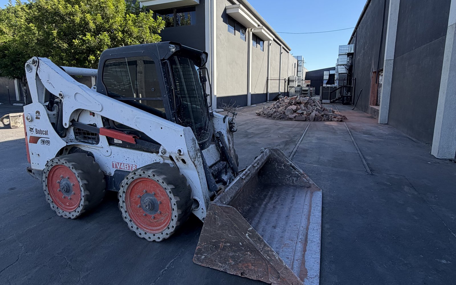 Bobcat skid steer working the alley beside the warehouse with broken concrete piled up
