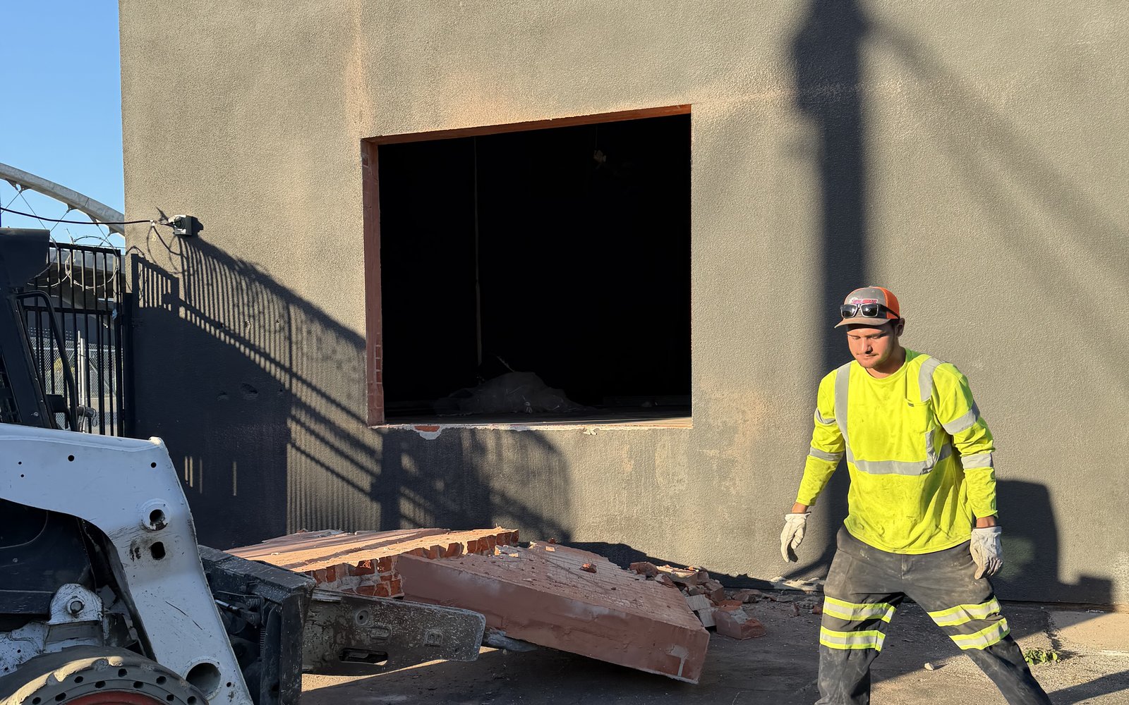 Crew member beside the Bobcat and the cut wall panel next to a fresh opening