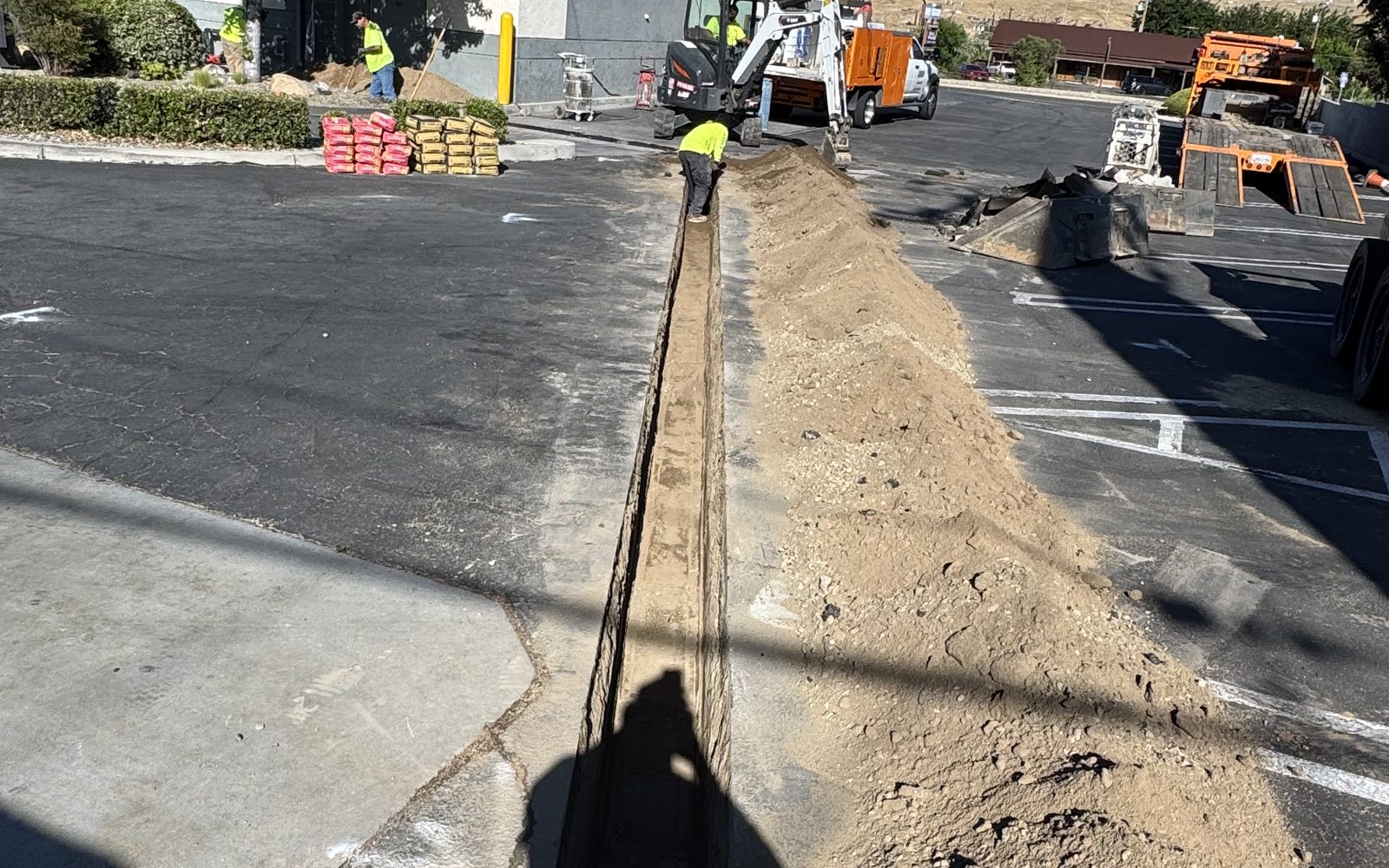 Long straight saw cut and open trench across an asphalt parking lot with spoil piled alongside