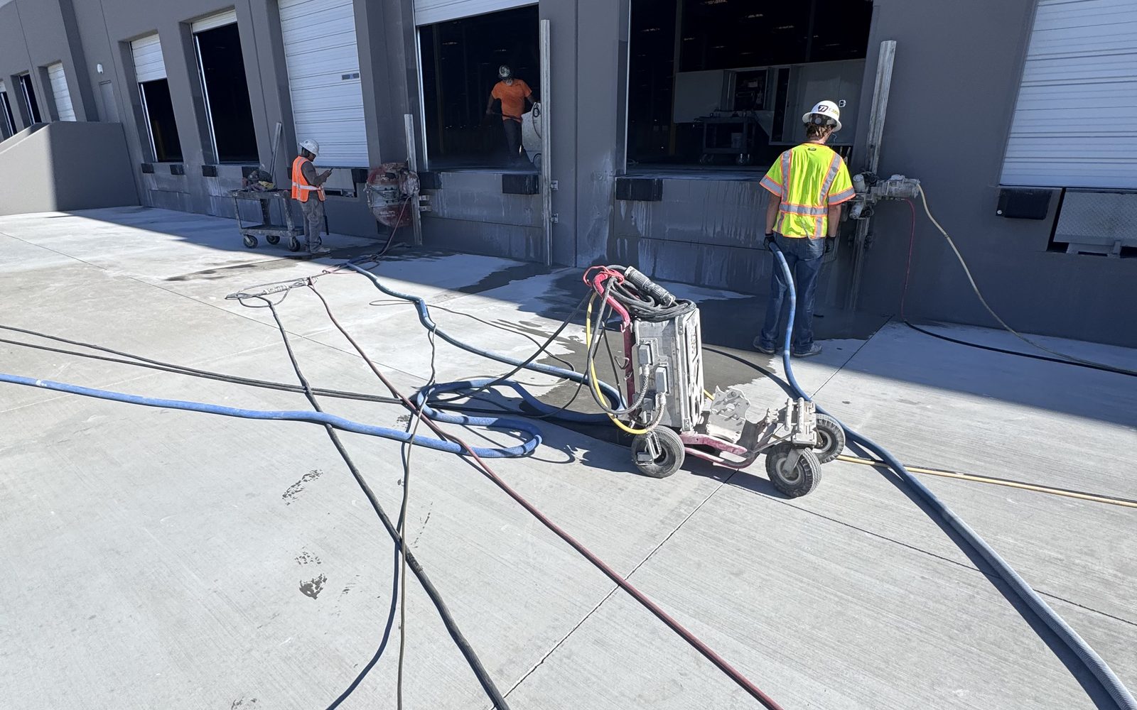 Worker in a hi-vis vest running a saw at a warehouse dock door with hoses across the concrete