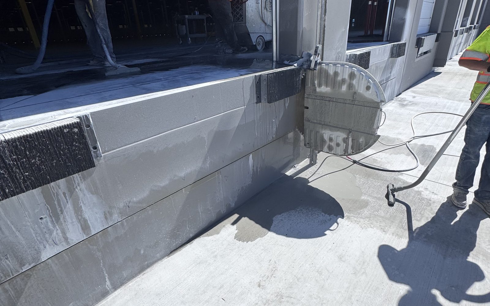 Wall saw on a track cutting a dock leveler pit while two workers work inside the warehouse